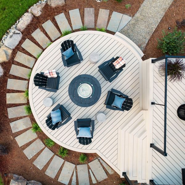 An extension of the backyard deck that is circular in the color Salt Flat with added deck chairs surrounding a Trex Fire Table.